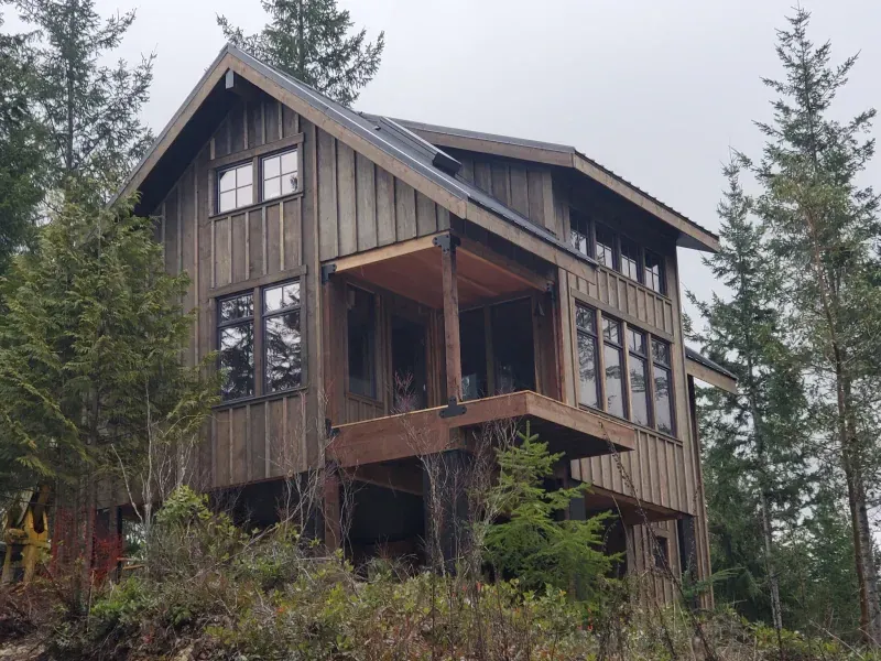 A small wooden house is surrounded by trees on a hillside