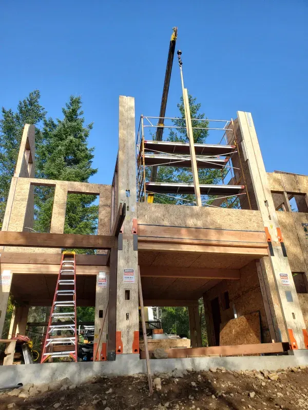 A crane is lifting a piece of wood into a house under construction.