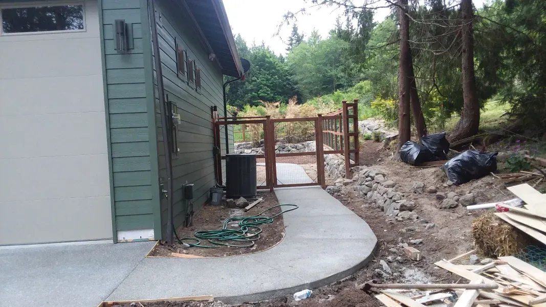 A concrete walkway leading to a garage with a wooden gate.