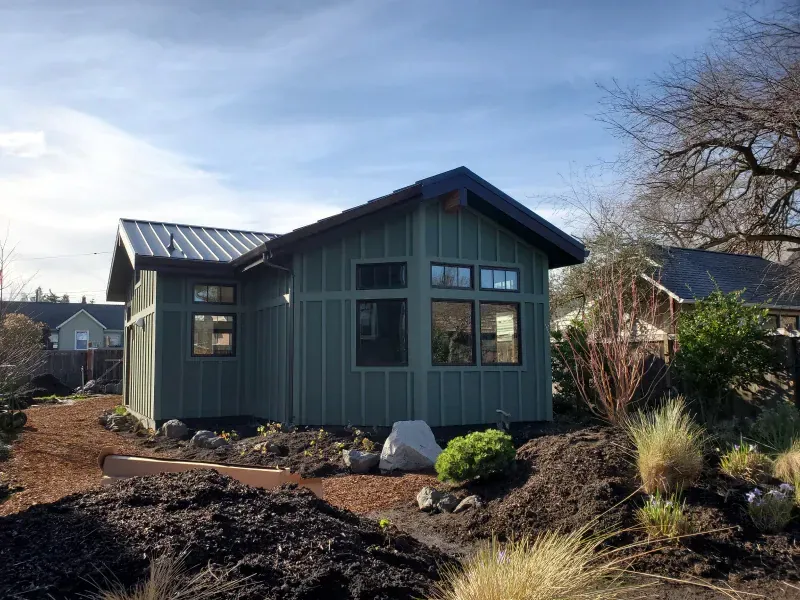 A small green house with a metal roof and a lot of windows