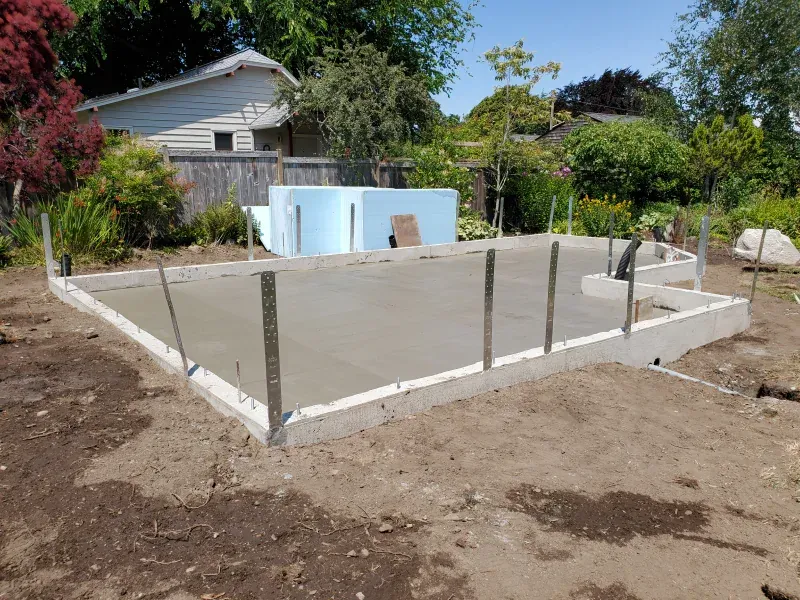A concrete base for a pool is being built in the backyard of a house.