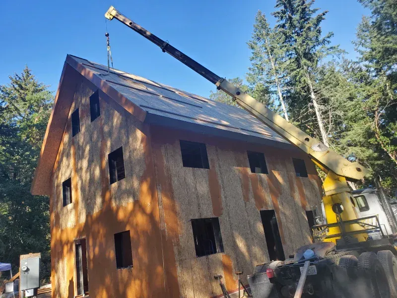 A crane is lifting the roof of a house under construction.
