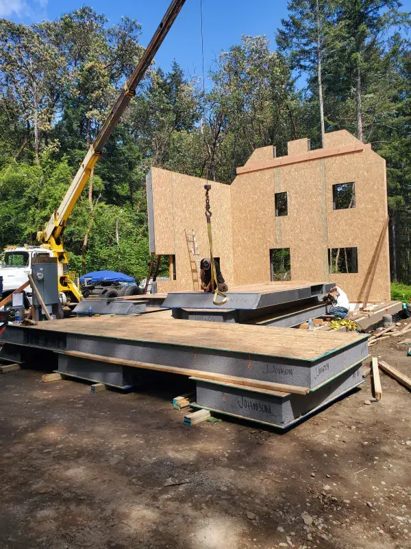 A crane is lifting a piece of wood in front of a house under construction