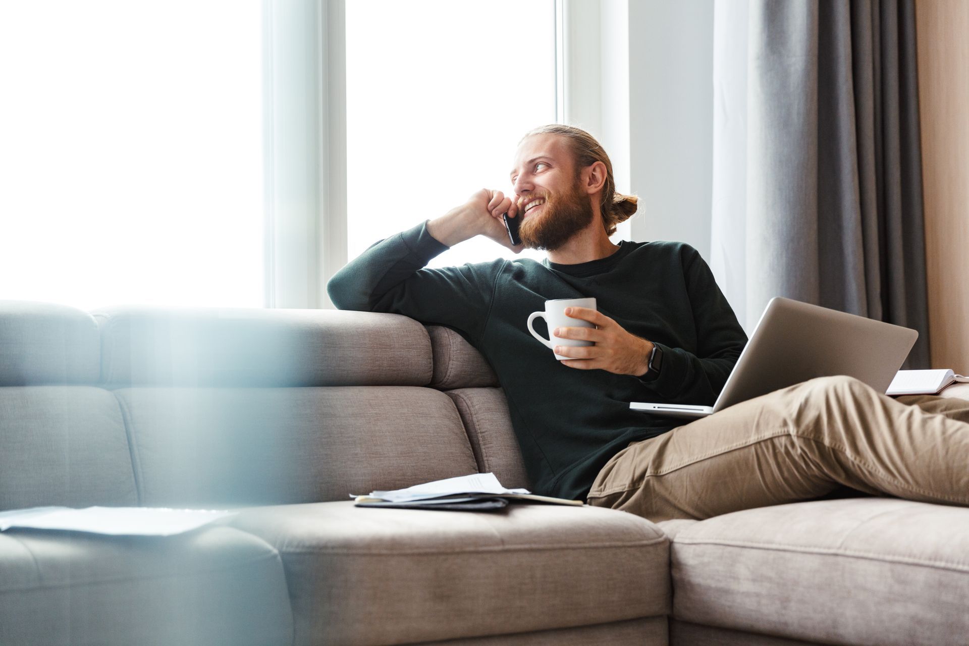 Un homme est assis sur un canapé avec un ordinateur portable et une tasse de café.