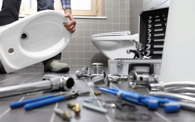 A Plumber Is Installing A Toilet In A Bathroom — ARK Plumbing & Gasfitting In Moss Vale, NSW
