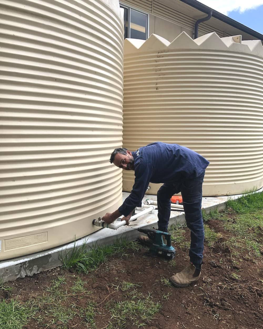 A Man Is Working On A Water Tank Outside Of A Building — ARK Plumbing & Gasfitting In Exeter, NSW