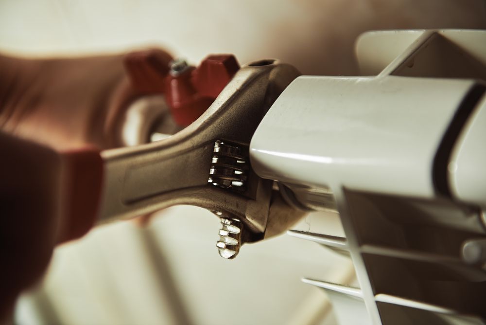 A Person Is Fixing A Radiator With A Wrench — ARK Plumbing & Gasfitting In Moss Vale, NSW