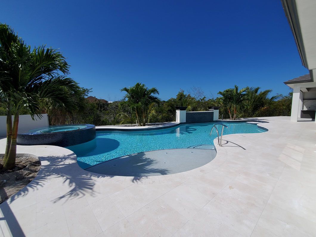 There is a large swimming pool in the backyard of a house surrounded by palm trees.