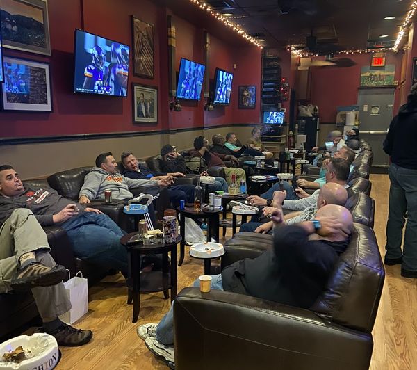 a group of men are sitting in a cigar lounge in franklin square  watching a game