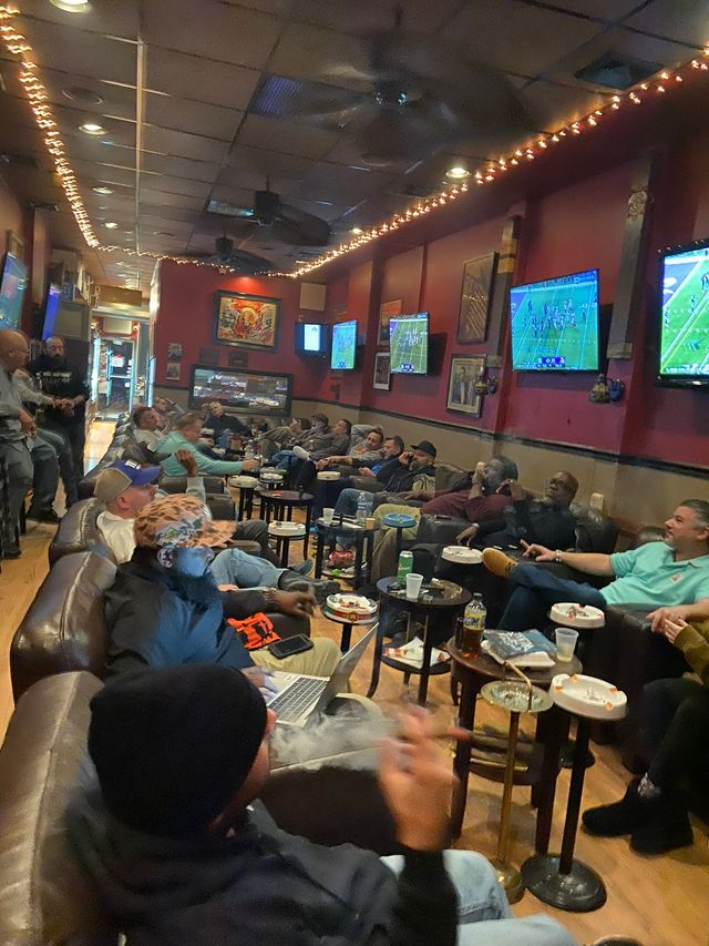 a group of men sit in a room watching a football game at a cigar lounge in nassau county
