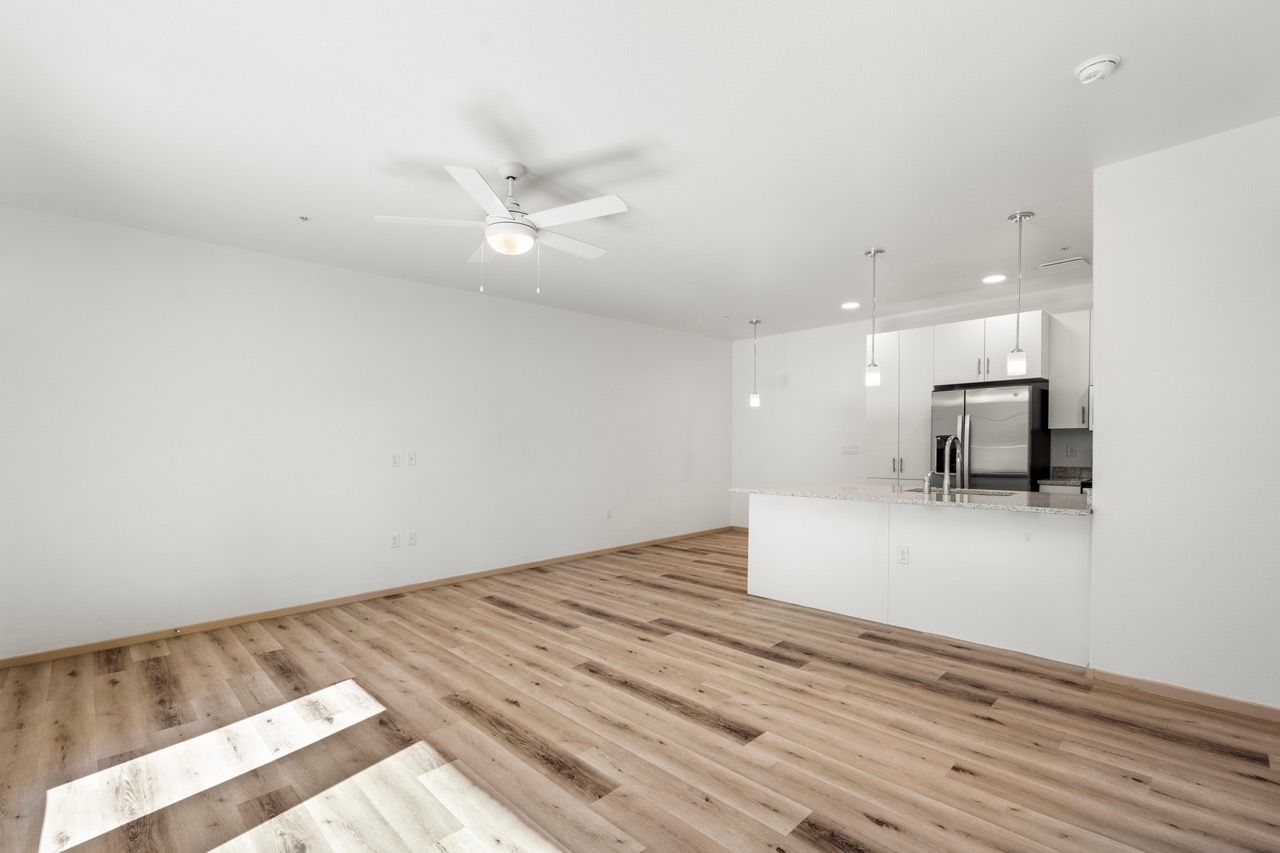 Empty modern apartment living area with a kitchen island, pendant lights, and stainless steel appliances.