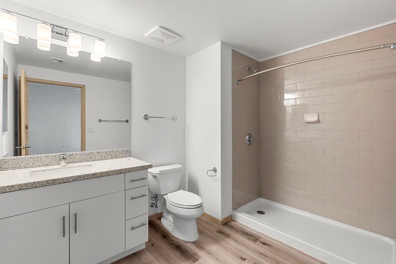 Bathroom with a white vanity, mirror, toilet, and beige-tiled shower.