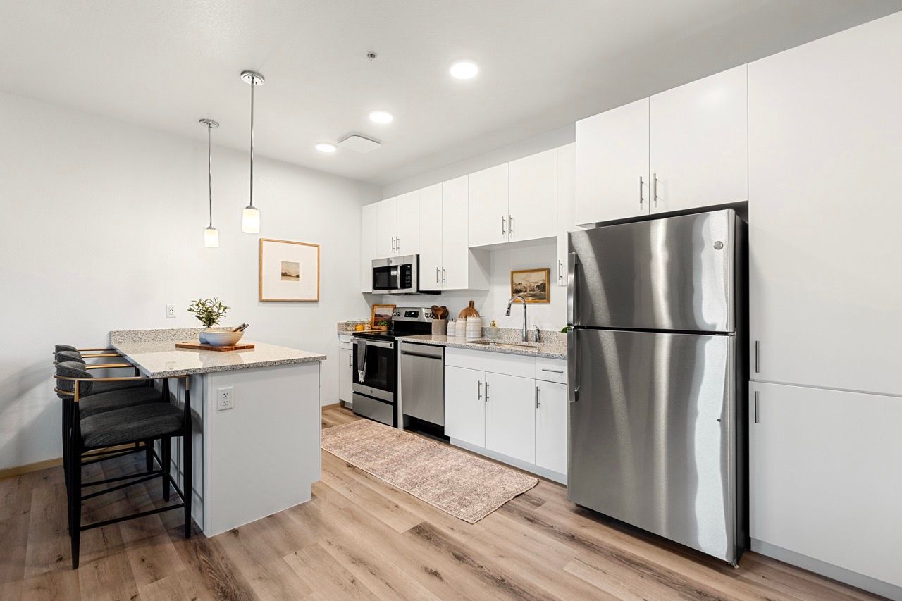 Modern kitchen with white cabinets, granite countertops, stainless steel fridge, and island with bar stools.