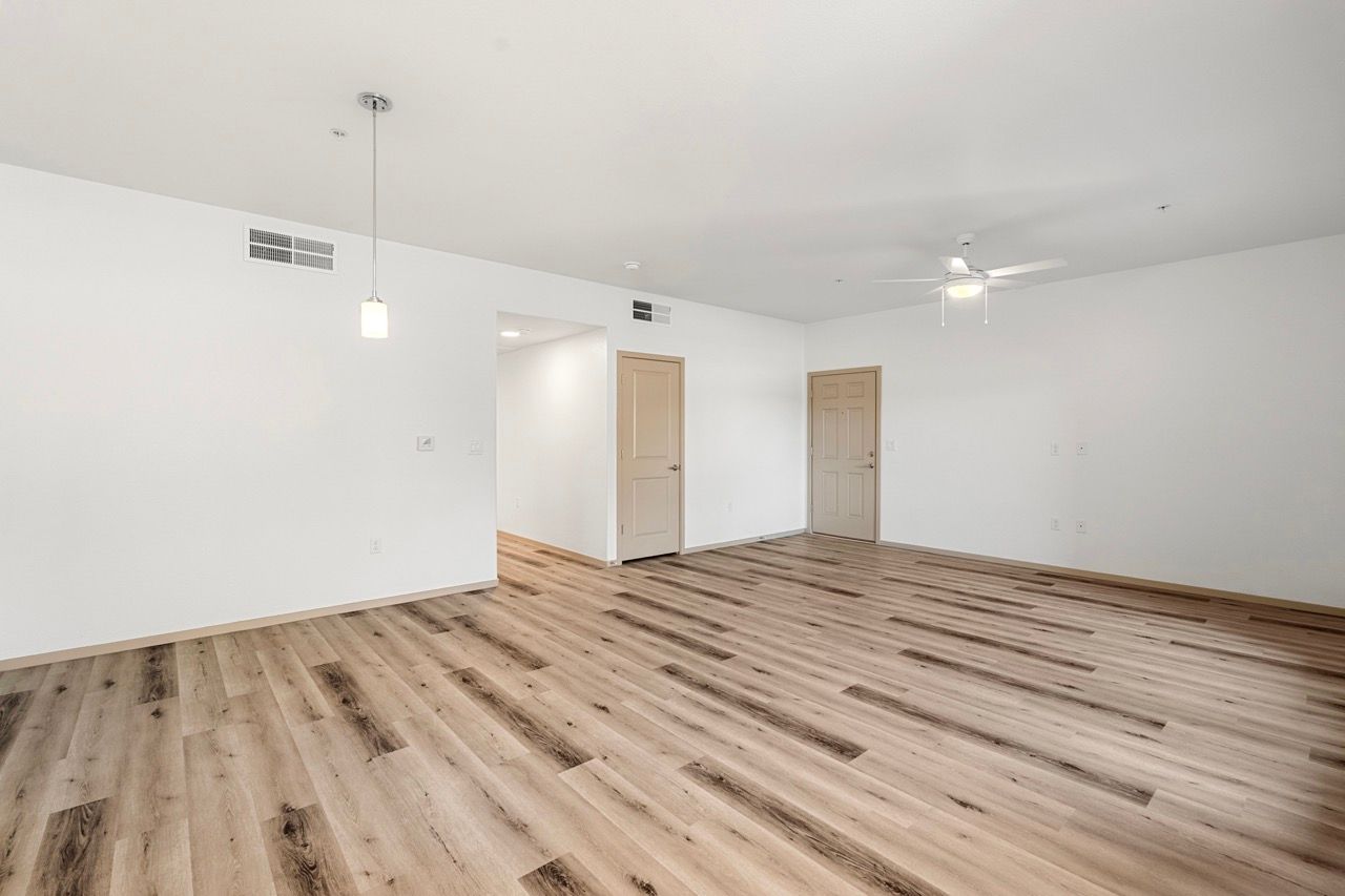 Bright empty living room with wood-look flooring, white walls, and a ceiling fan.