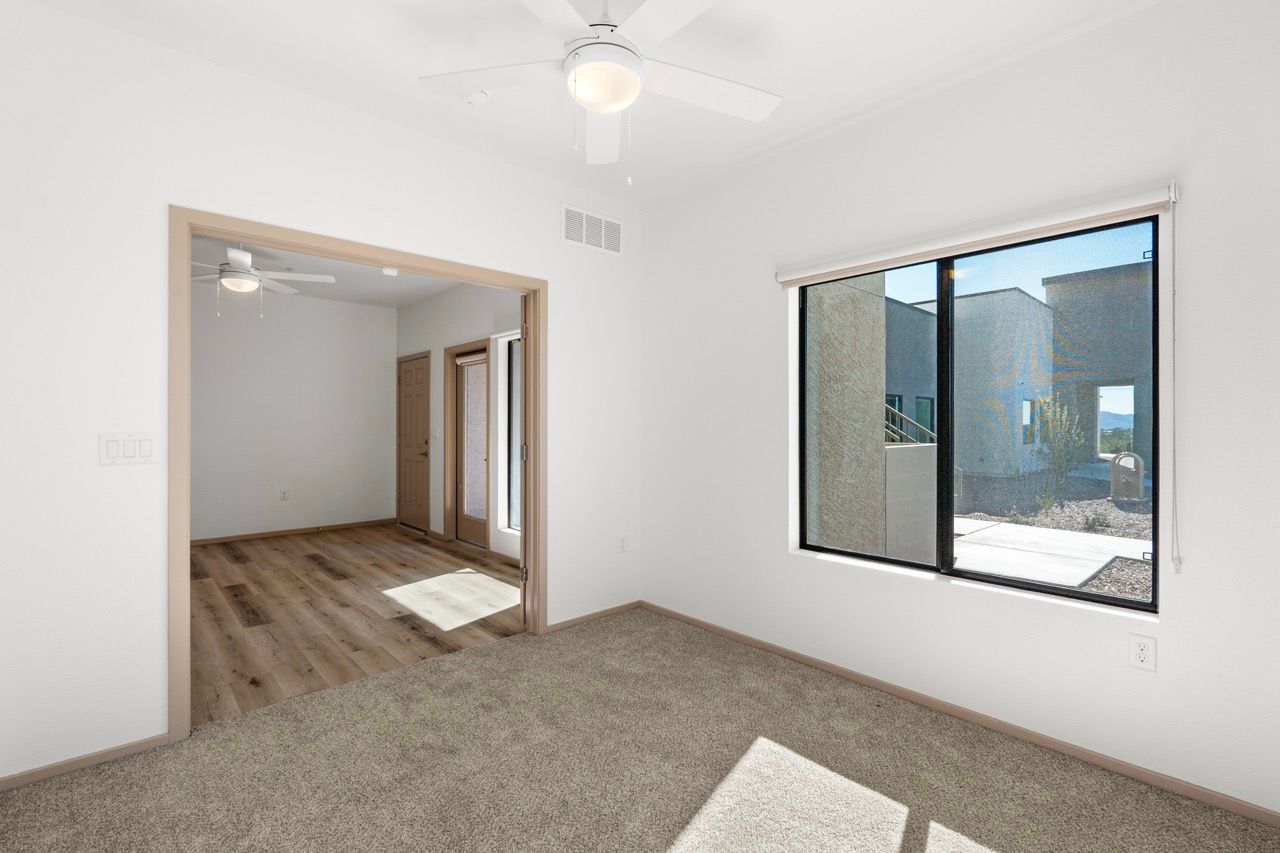 Bright bedroom with window, ceiling fan, and doorway to a wood-floored living area.