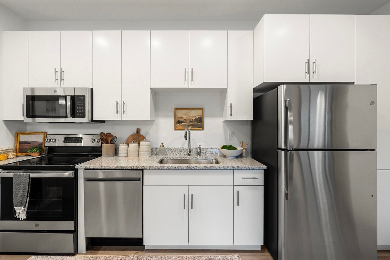Modern apartment kitchen with white cabinets and stainless steel appliances.