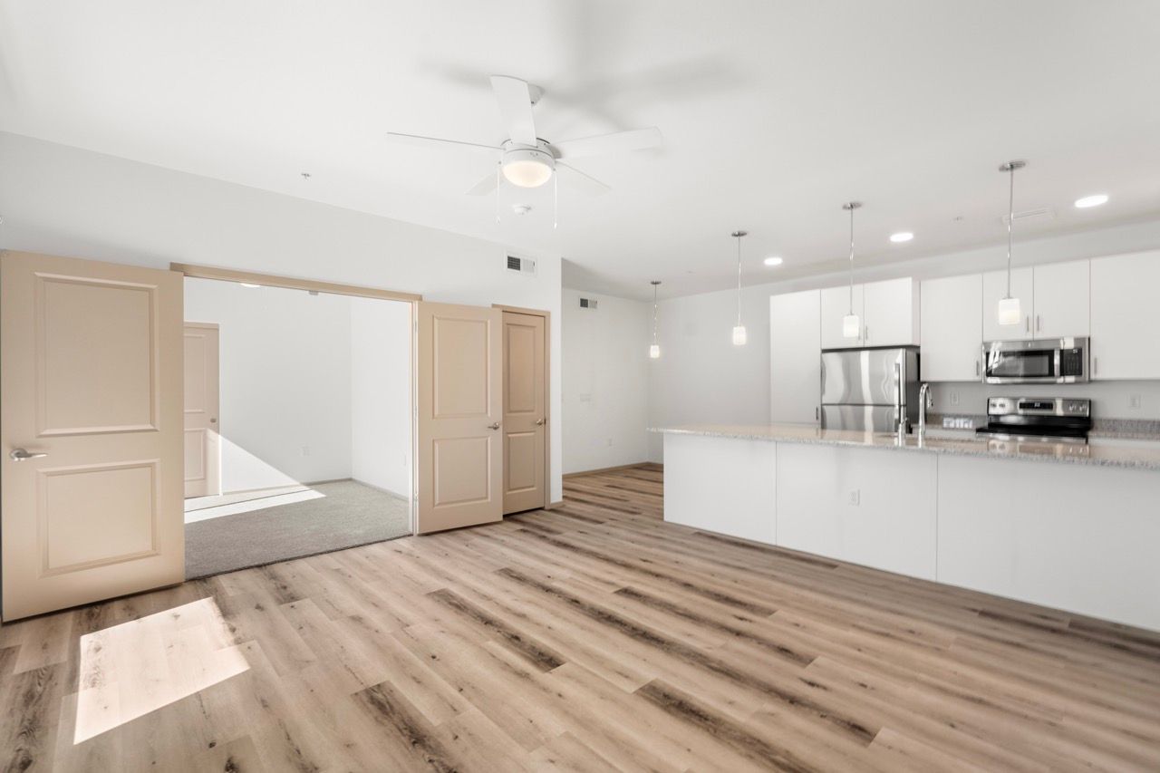 Bright modern kitchen and open-concept living area with island, white cabinets, and stainless steel appliances.
