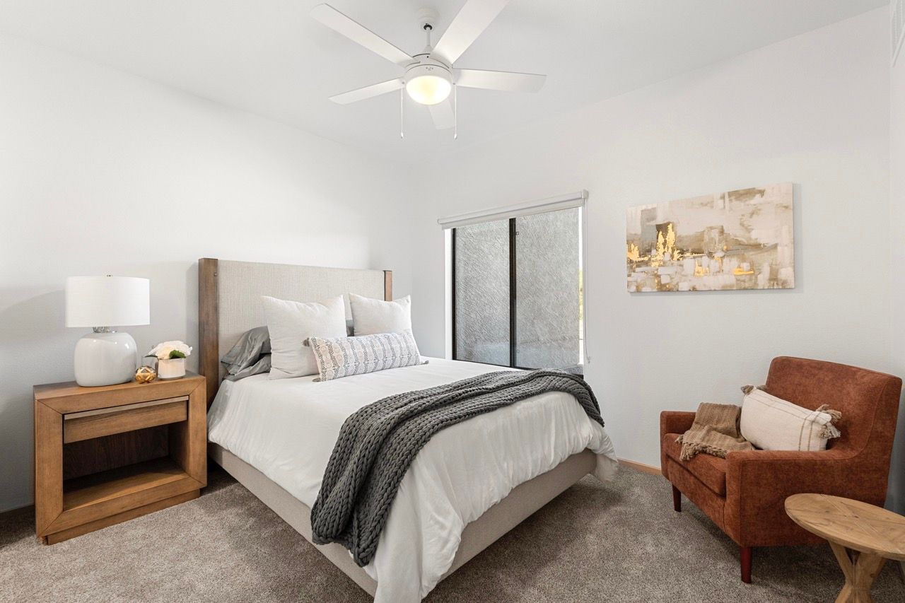 Bedroom in a modern apartment with a bed, nightstand, lamp, and rust-colored chair.