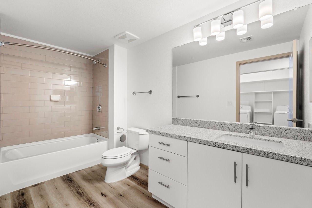 Bathroom with tub/shower, toilet, granite vanity, and nearby laundry area visible through the doorway.
