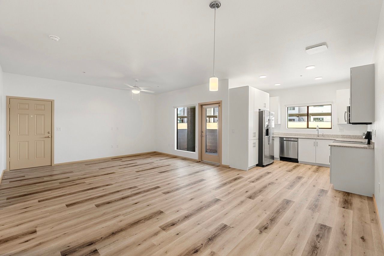 Open living area with light wood floors, white walls, and a modern kitchen.