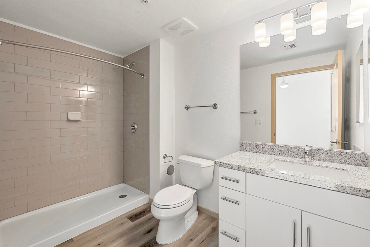 Modern apartment bathroom with a tub/shower, toilet, and white vanity.