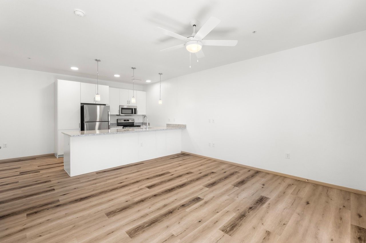 Open-concept kitchen with island, white cabinets, stainless appliances, and wood-look flooring.