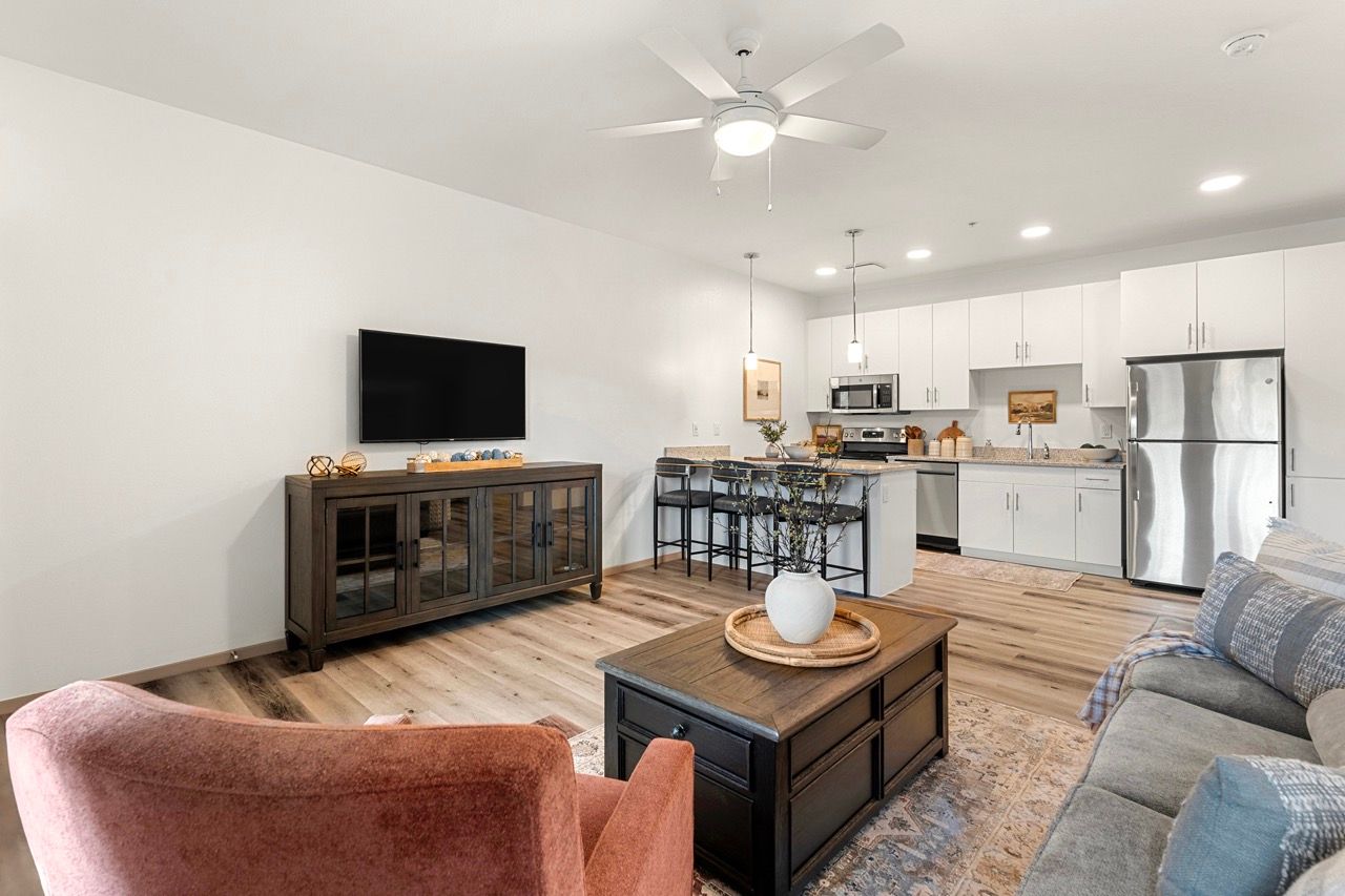 Open-concept living room and kitchen in a modern apartment with white cabinets and stainless appliances.