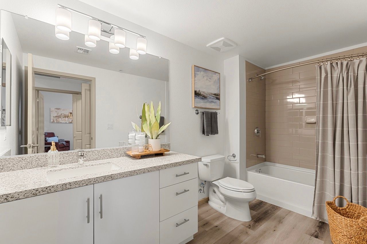Bright apartment bathroom with double vanity, large mirror, toilet, and bathtub/shower.