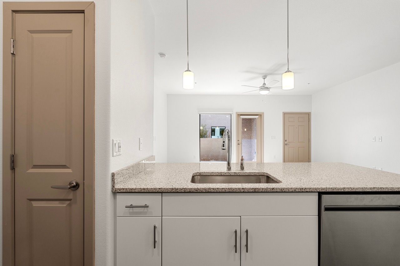 Open-concept kitchen with granite island, stainless sink, pendant lighting, and adjacent living area.