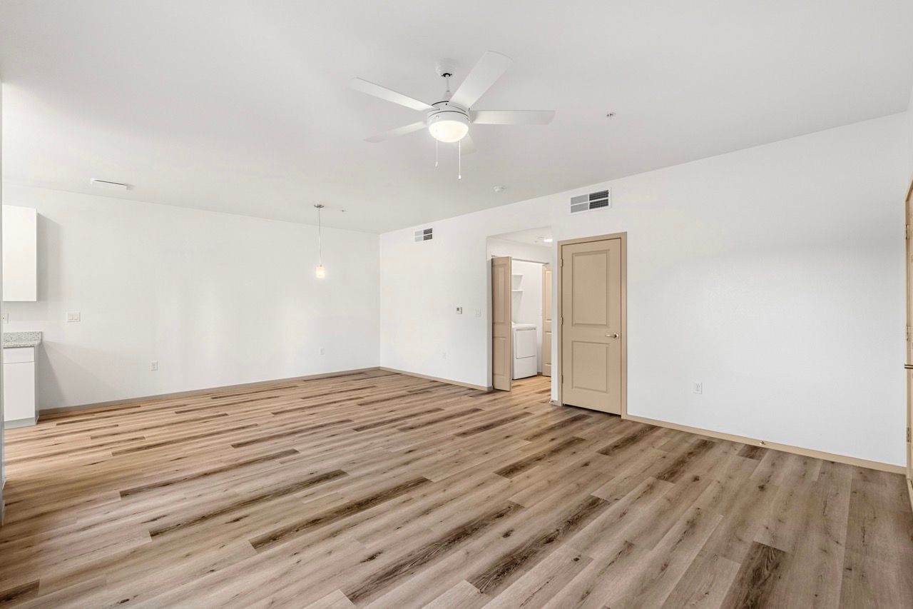 Bright open living area with white walls, ceiling fan, and wood-look flooring.