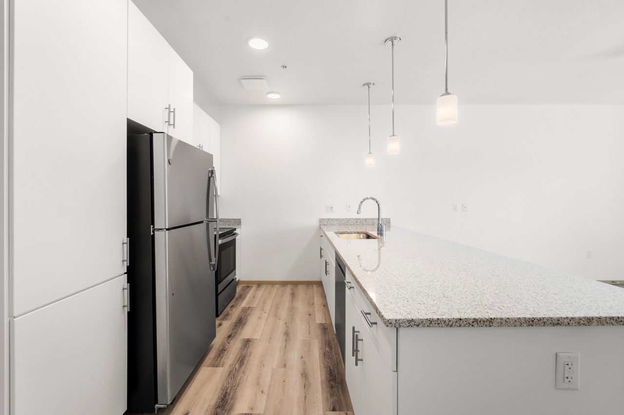 Bright, contemporary apartment kitchen with white cabinets, granite countertops, island, and stainless steel appliances.