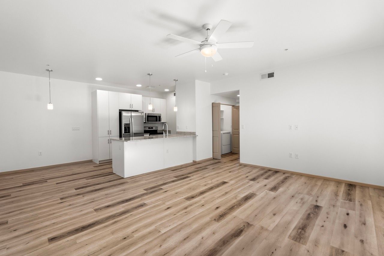Open-concept kitchen and living area with white cabinets, island, stainless appliances, and wood floors.