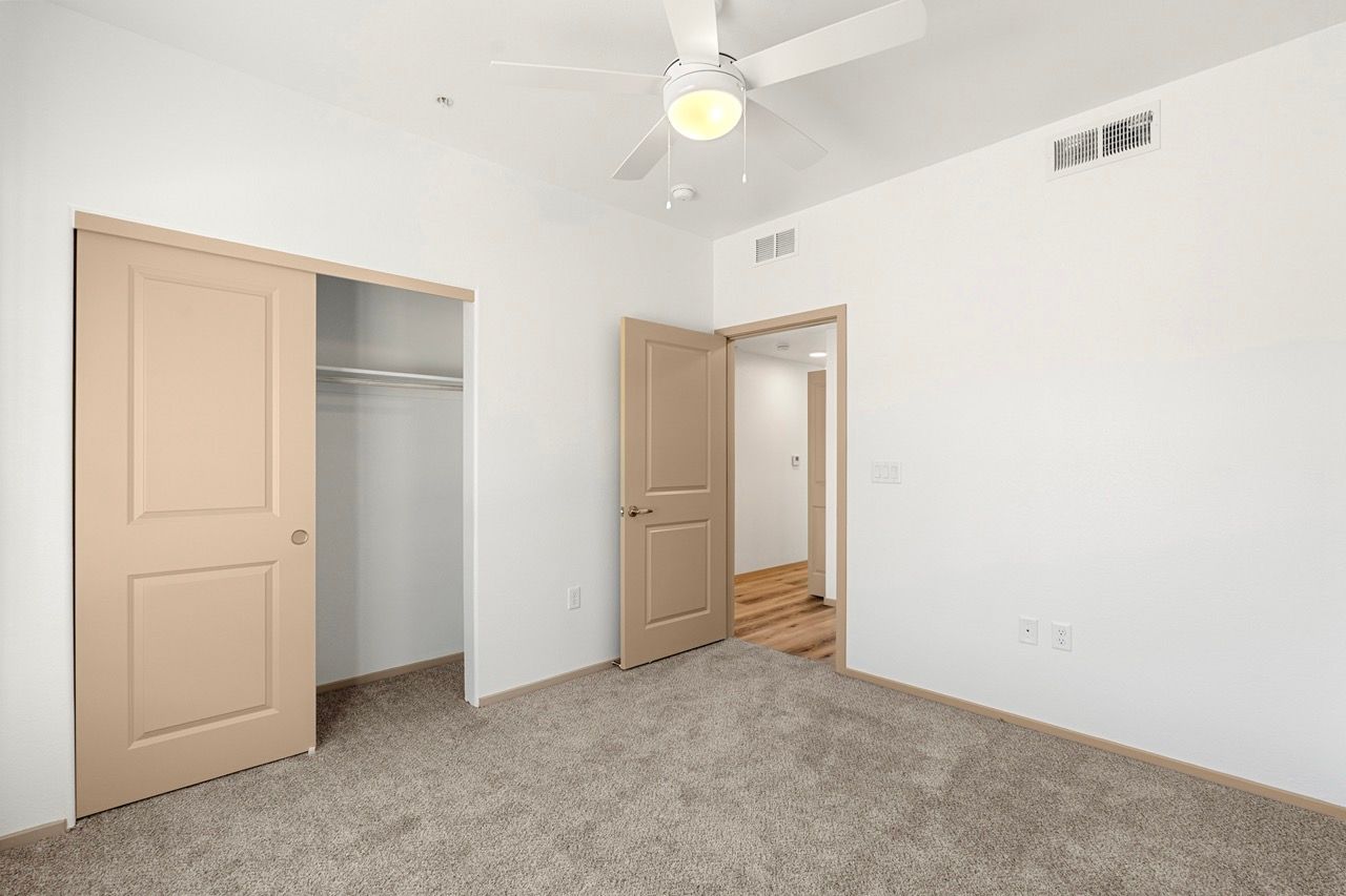 Bedroom with beige closet doors, neutral walls, carpet, and a ceiling fan.