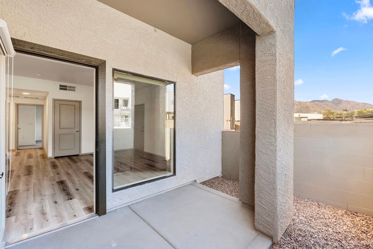 Patio with a sliding glass door leading into a modern apartment with wood-look flooring.