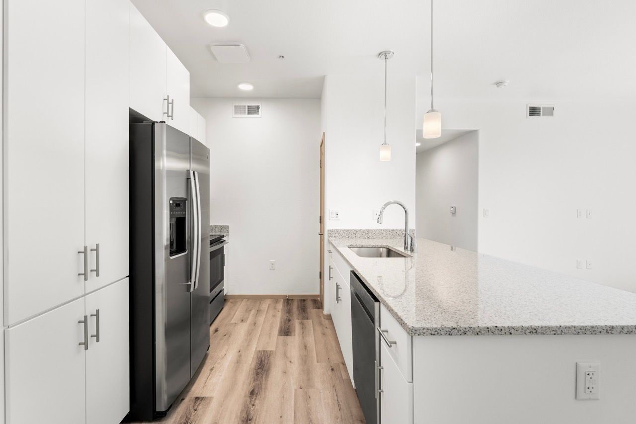 Modern kitchen in a white-cabinet apartment with stainless steel fridge and granite counters.
