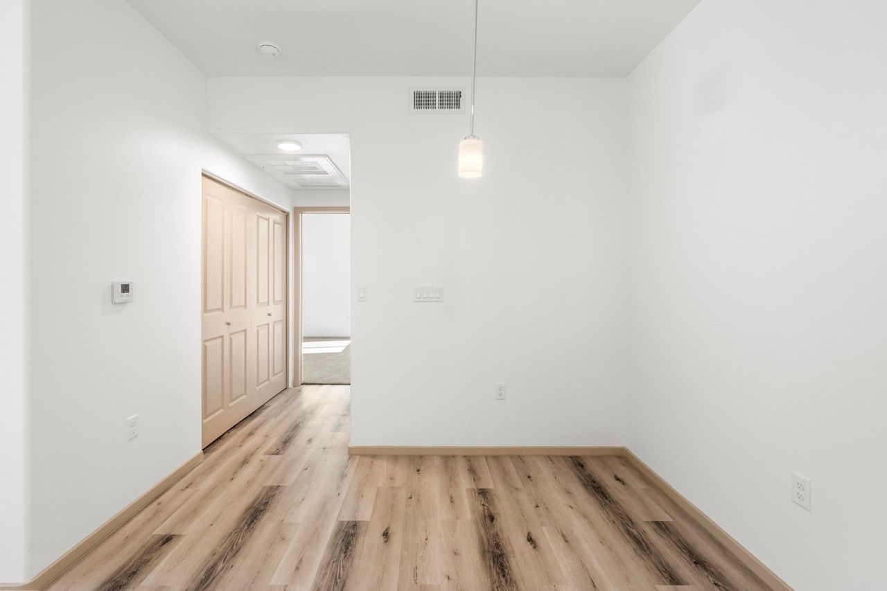 Empty apartment room with white walls, wood-like flooring, and a doorway.