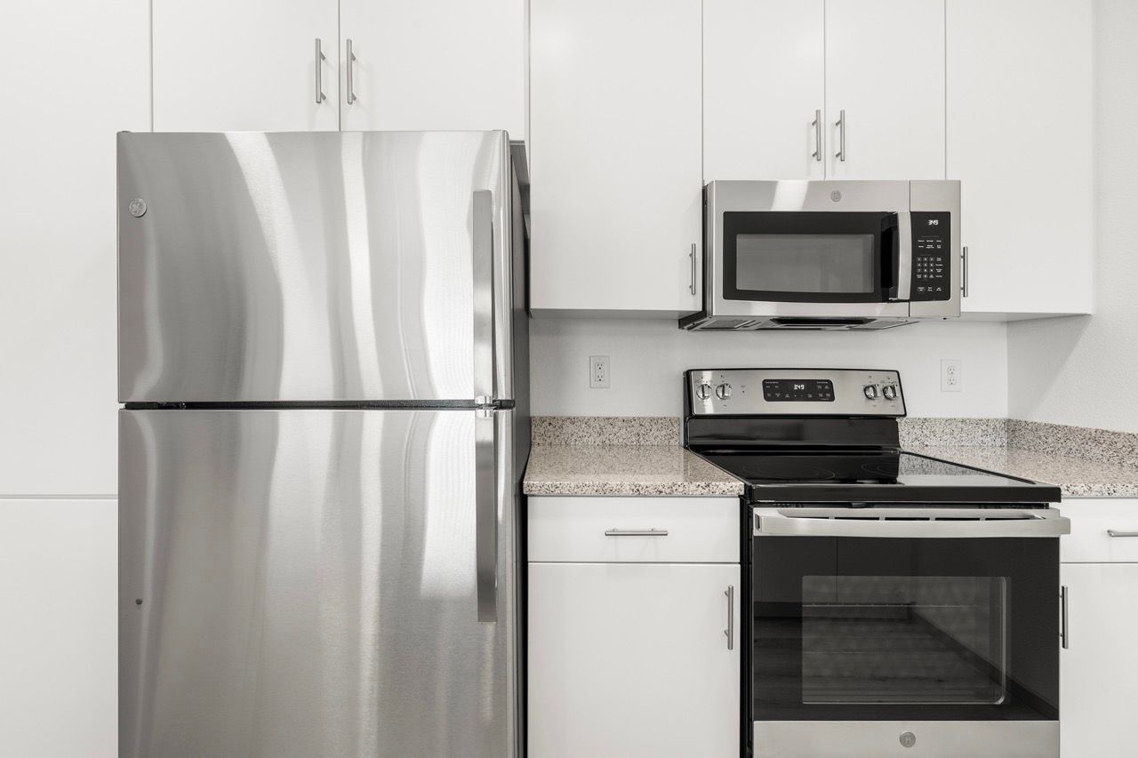 Stainless steel refrigerator, microwave, and range in a white kitchen.