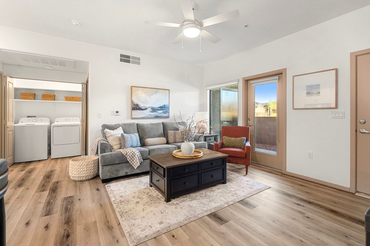 Living room in an apartment with a sofa, coffee table, ceiling fan, and a visible laundry area.
