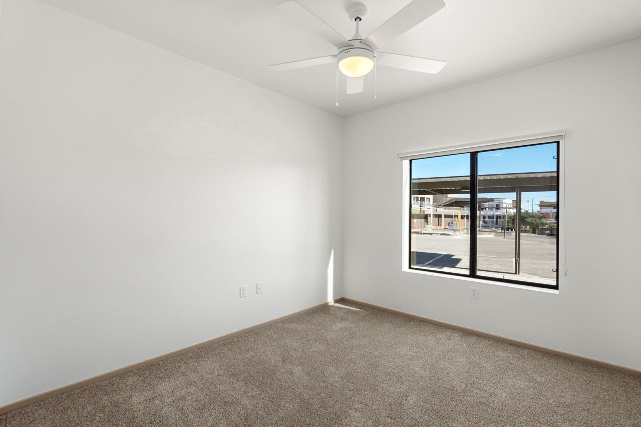 Empty bedroom with beige carpet, white walls, a window, and a ceiling fan.