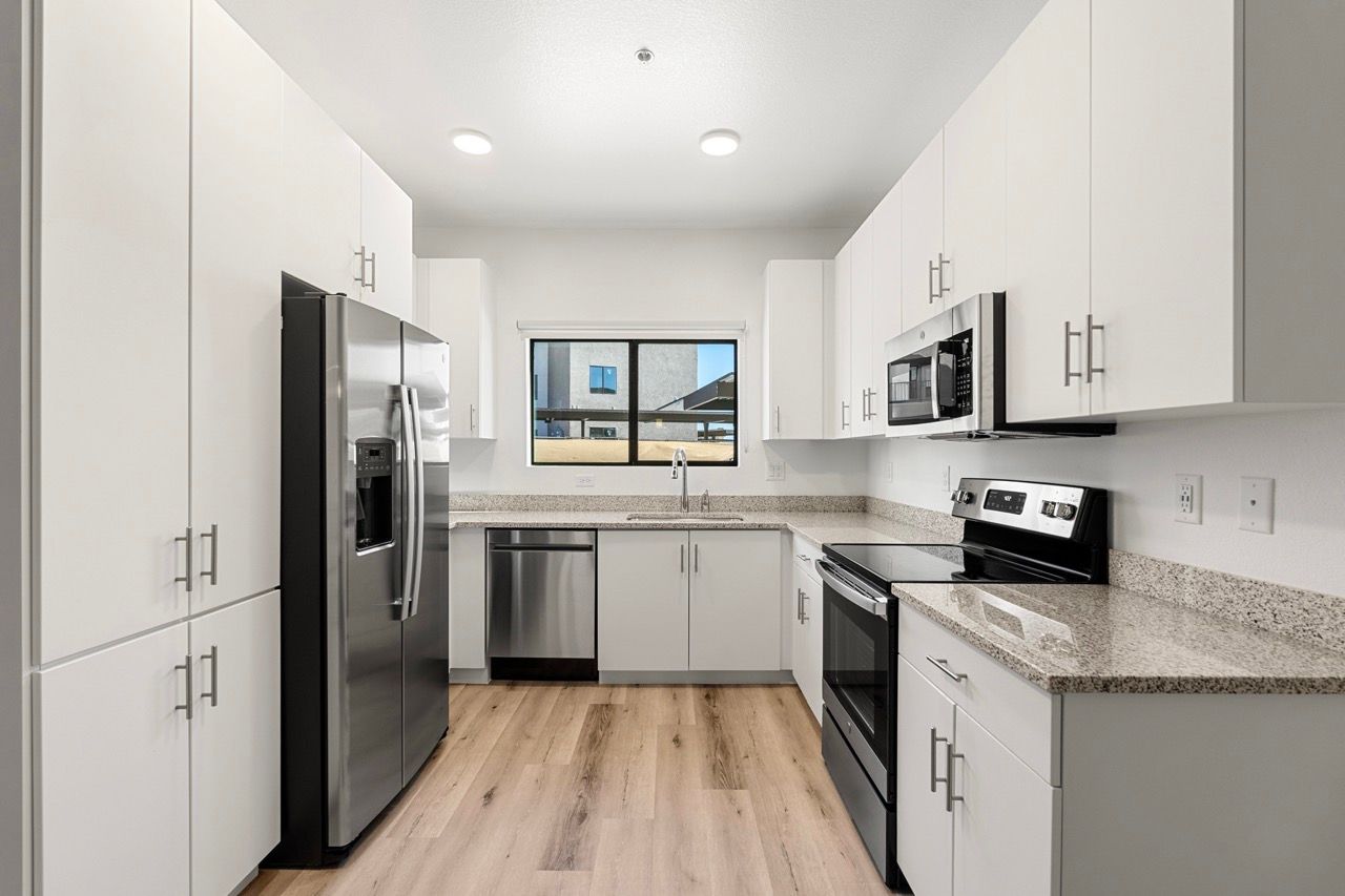 Modern white kitchen with stainless steel fridge, oven, microwave, and a window above the sink.