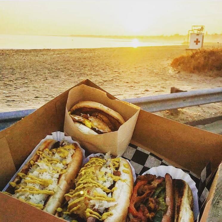 A box of hot dogs and a hamburger on the beach.