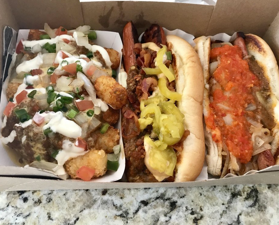 Three hot dogs in a cardboard box with different toppings