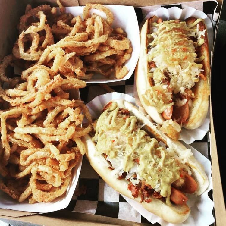 A box of hot dogs and onion rings on a checkered table cloth