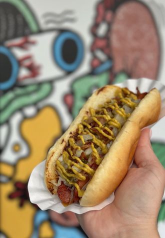 A person is holding a hot dog with mustard and onions on a paper plate.