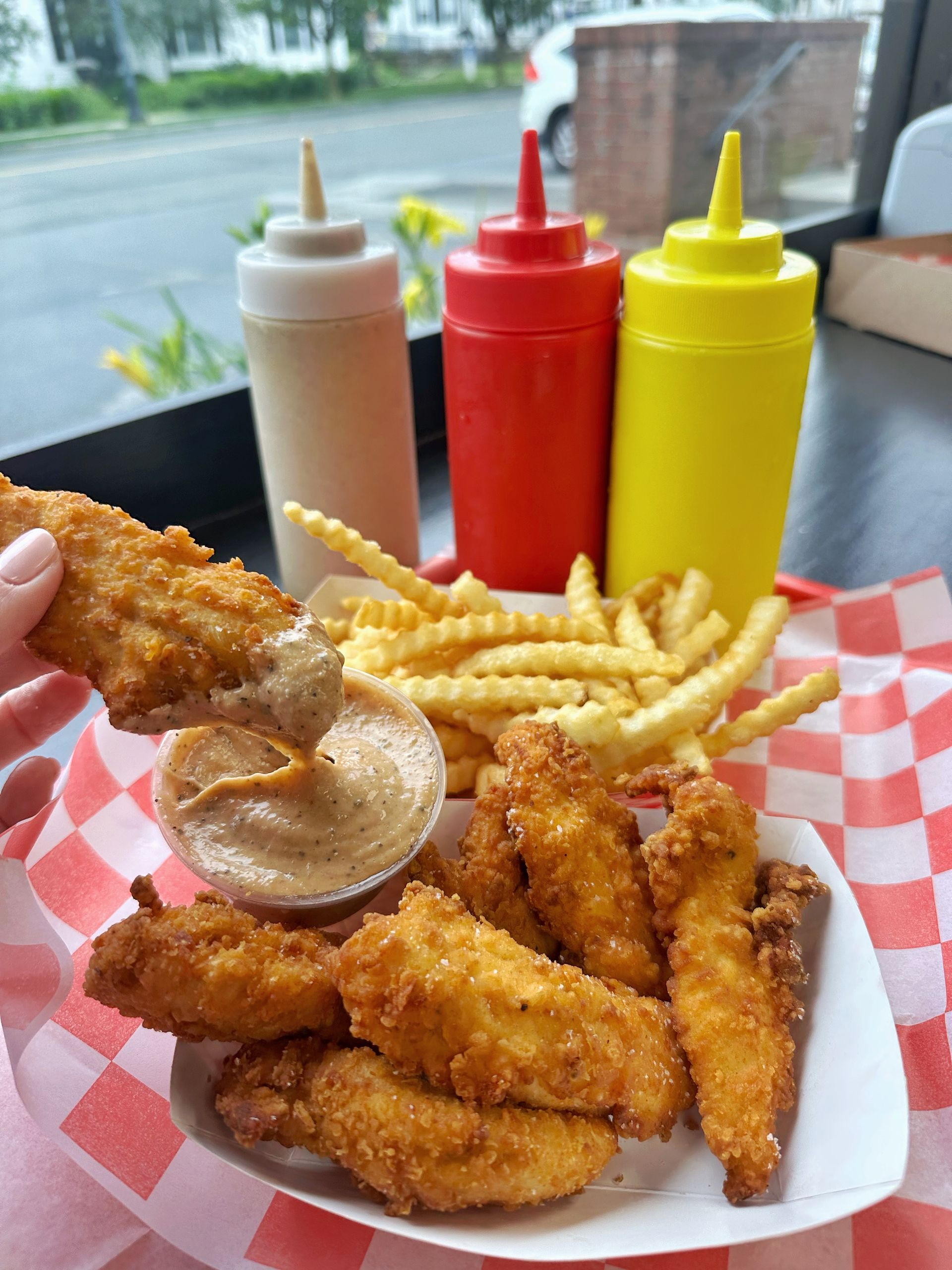 A person is holding a piece of fried chicken and french fries.