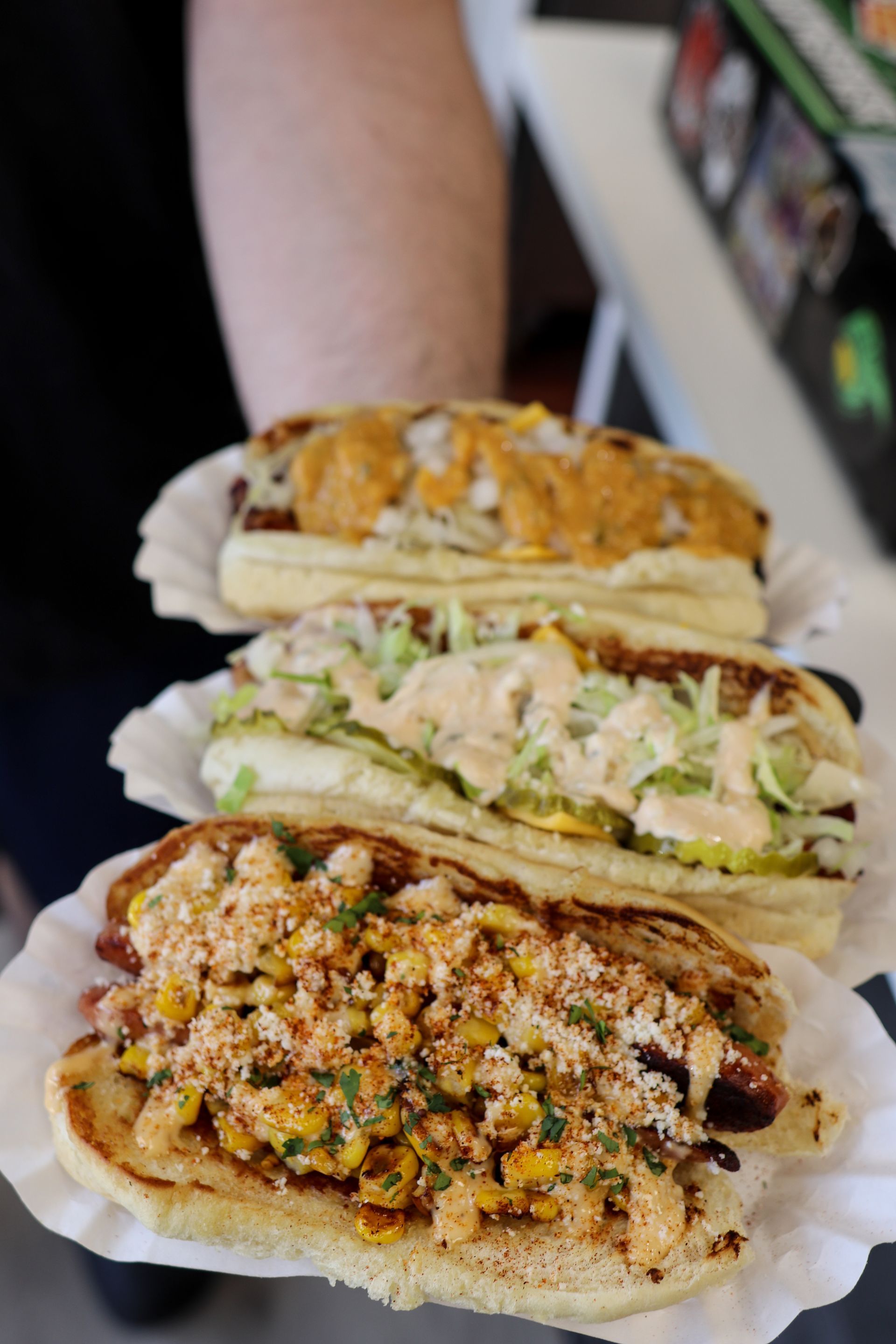 A person is holding three hot dogs on paper plates.