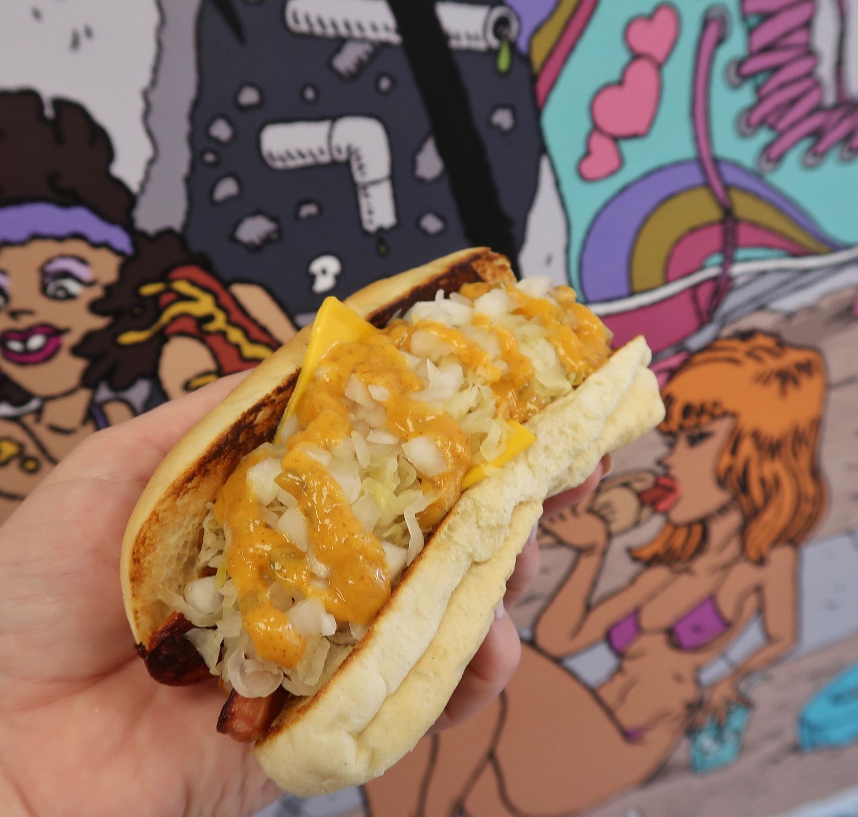 A person is holding a hot dog with cheese and cabbage