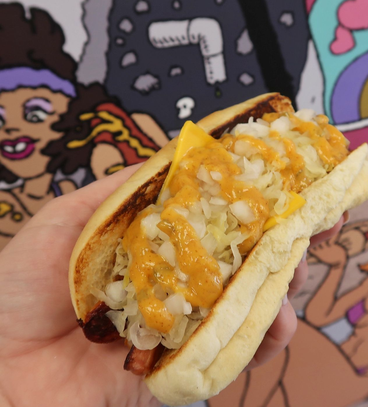 A person is holding a hot dog with cheese and cabbage