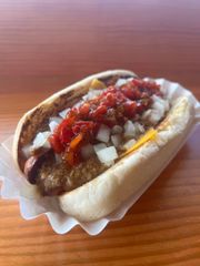 A hot dog with tomato sauce and onions on a bun on a wooden table.