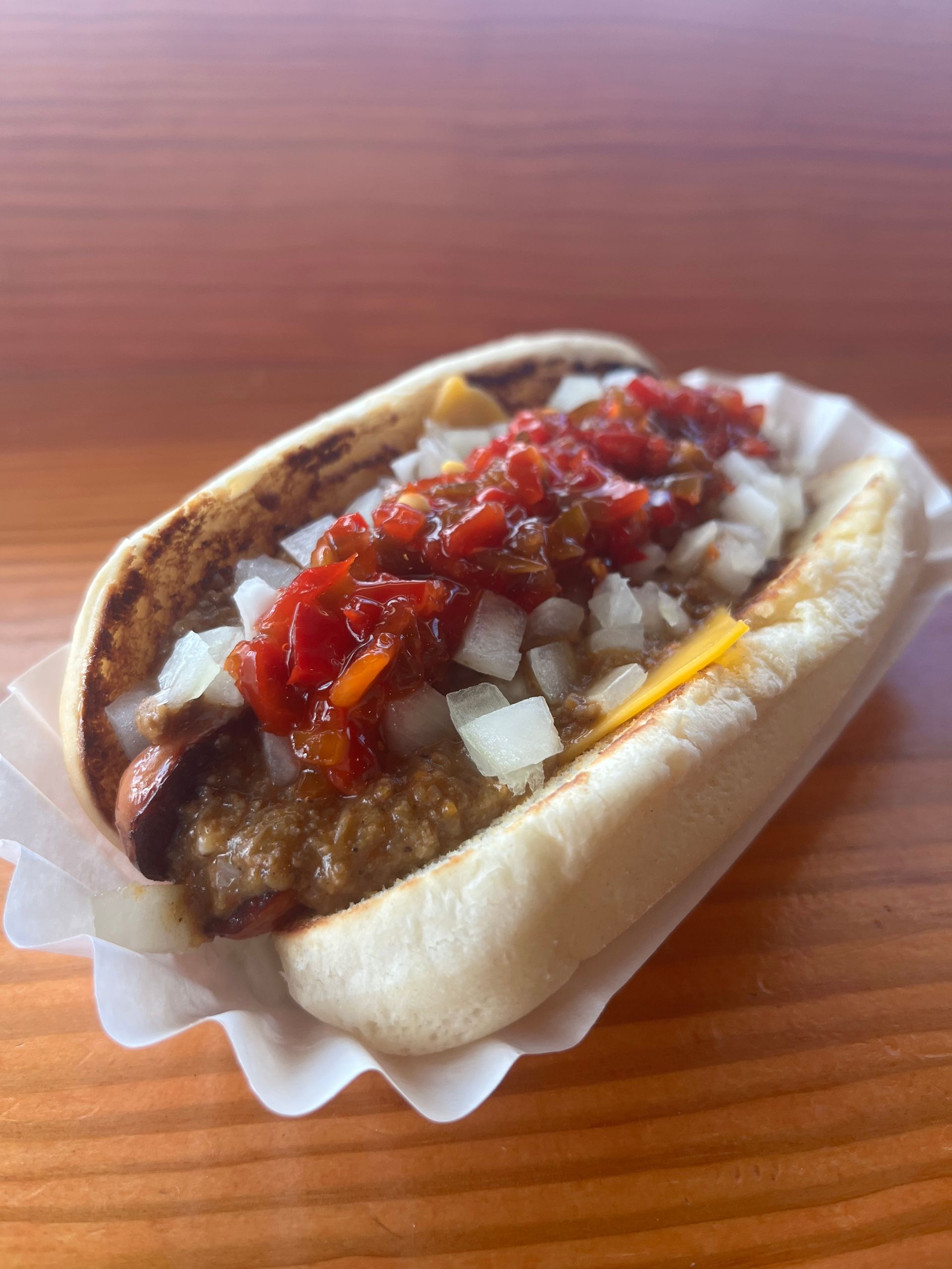 A hot dog with tomato sauce and onions on a bun on a wooden table.